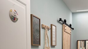 Ein Flur mit einer Schiebetür, einer an der Wand montierten Überwachungskamera, einem gerahmten Bild, einer aufhängbaren Tragetasche und einer Bank mit Kissen.