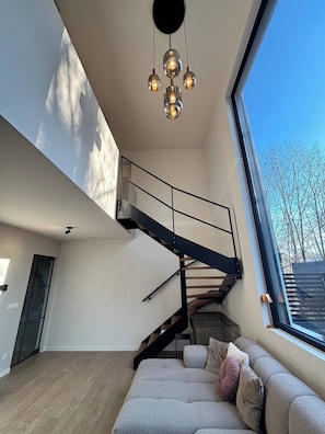 A modern interior with a staircase, a sofa, and a large window. - Luxury Home in Hoge Kempen National Park With Swimming Pool (Genk)
