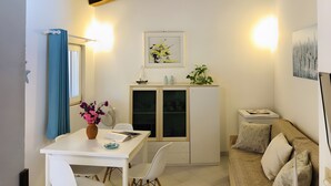 A compact living space with a dining table, chairs, a sofa, a cabinet with glass doors, and a ceiling with exposed beams. - Bouganville Two-Room Apartment 80 m from the Beach with Private Terrace, Garden & AC (Porto Taverna)