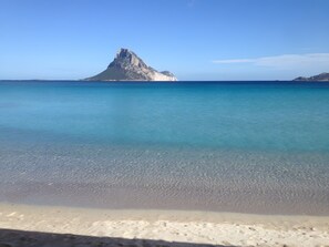 A beach with clear water and a mountain in the background.