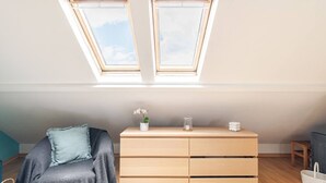 A room with a skylight, a bed with a blue pillow, a wooden dresser, and a small table. - Cosy Loft Heart Of The City! (Lisboa)
