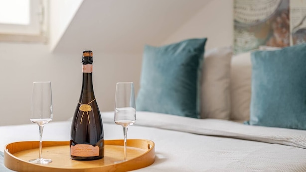 A bottle of wine on a tray with two glasses, set on a bed with pillows in a room with a window. - Cosy Loft Heart Of The City! (Lisboa)