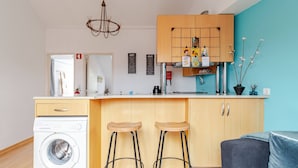 A compact kitchen with a washing machine, wooden stools, a bar area, and a blue wall. - Cosy Loft Heart Of The City! (Lisboa)