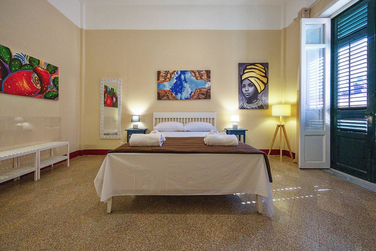 A hotel room with a bed, two bedside tables, a bench, and artwork on the walls.