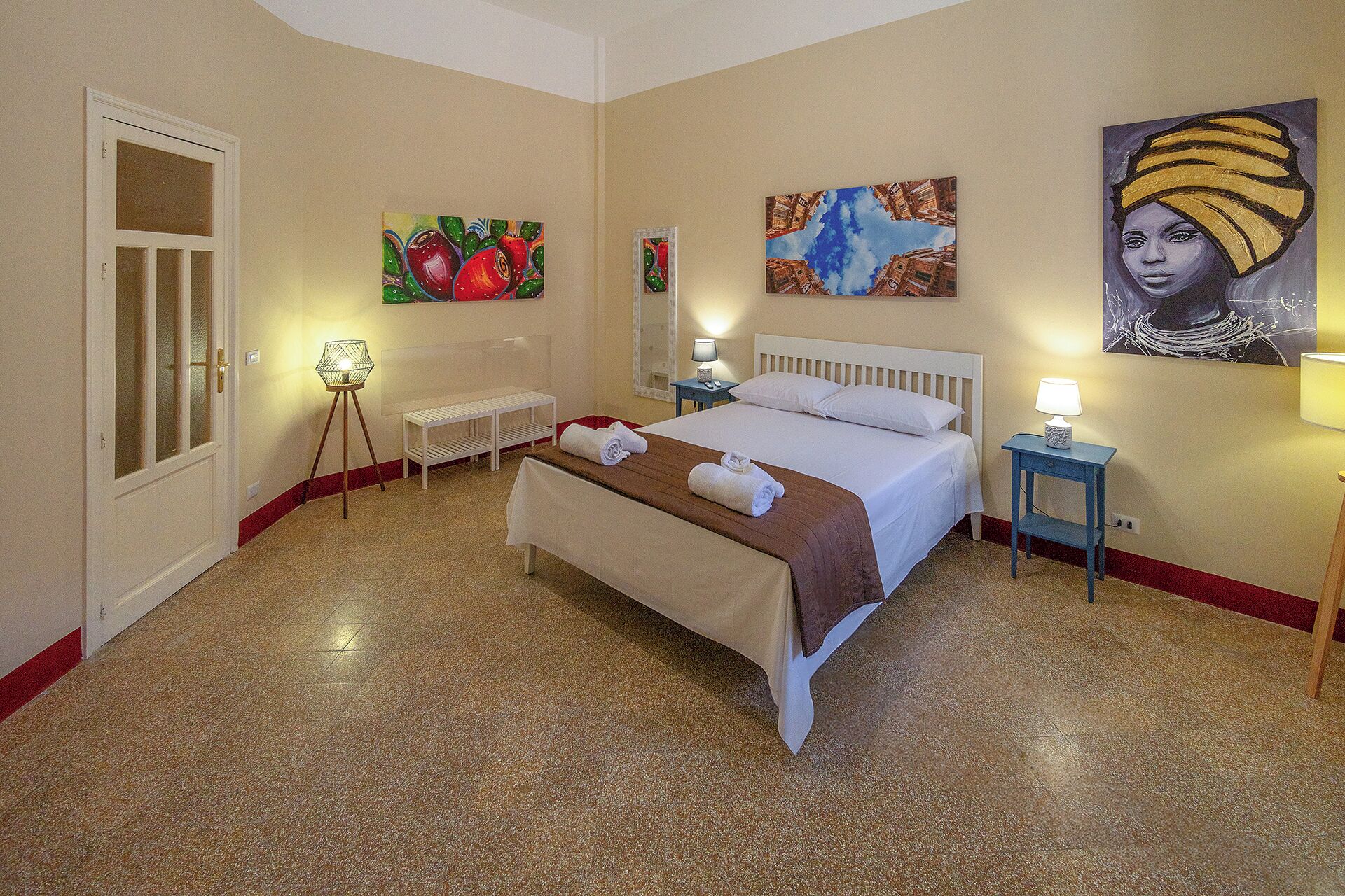 A hotel room with a bed, bedside tables, a chair, and artwork on the walls.