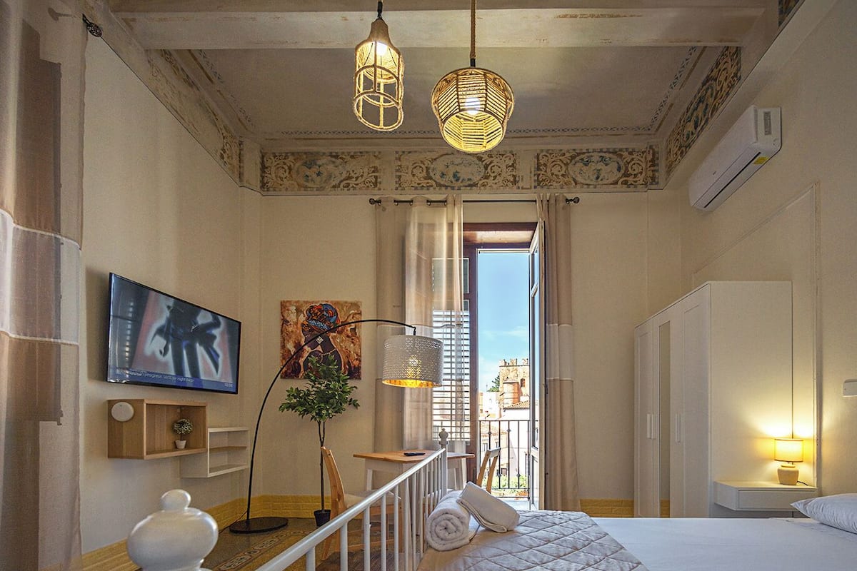 A hotel room with a bed, a TV, a painting, and a view of the city.