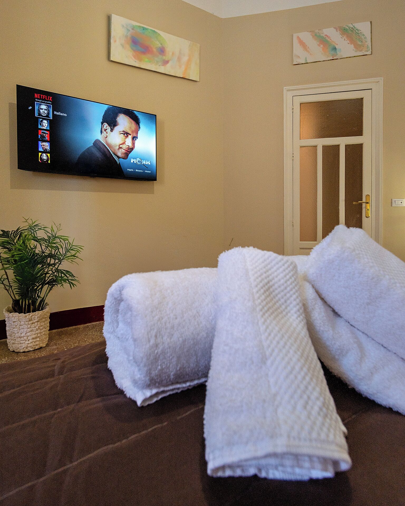 Une chambre d’hôtel avec une télévision diffusant un film, une plante en pot et des serviettes soigneusement pliées posées sur le sol.