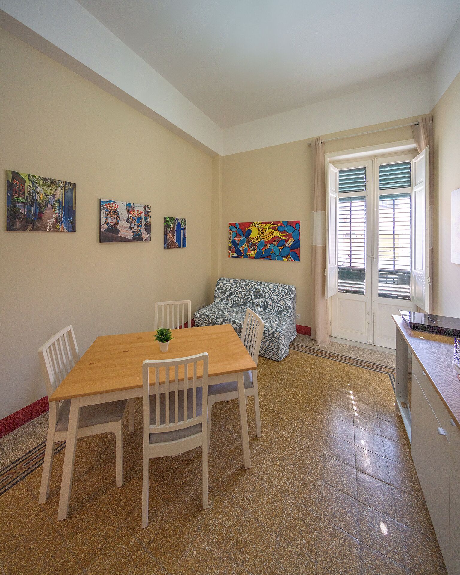 A dining area with a wooden table and chairs, a sofa, and a kitchen area with a countertop and cabinets.