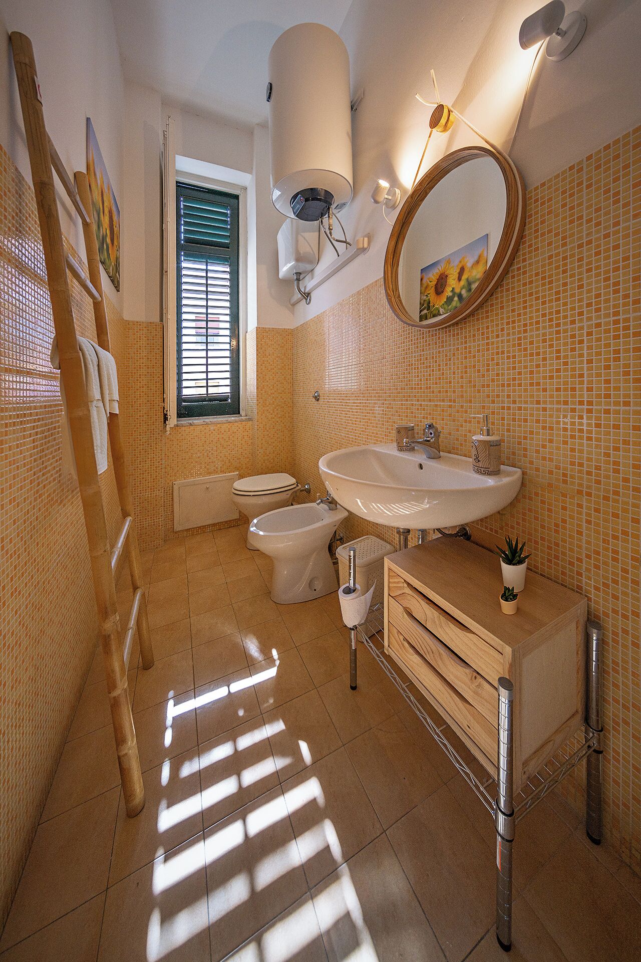 Een badkamer met toilet, bidet, wastafel en een spiegel met een zonnebloem schilderij.