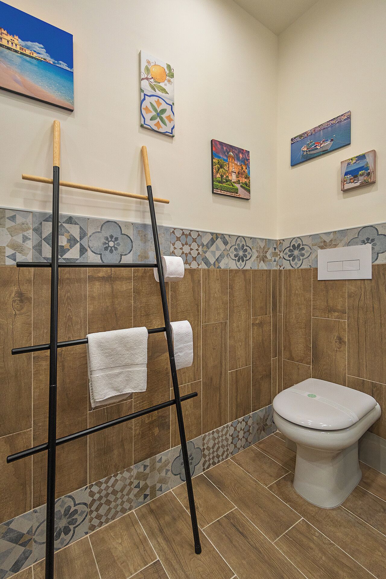 Ein Badezimmer mit Holzboden, Toilette, Handtuchhalter mit zwei Handtüchern und dekorativen Wandfliesen.
