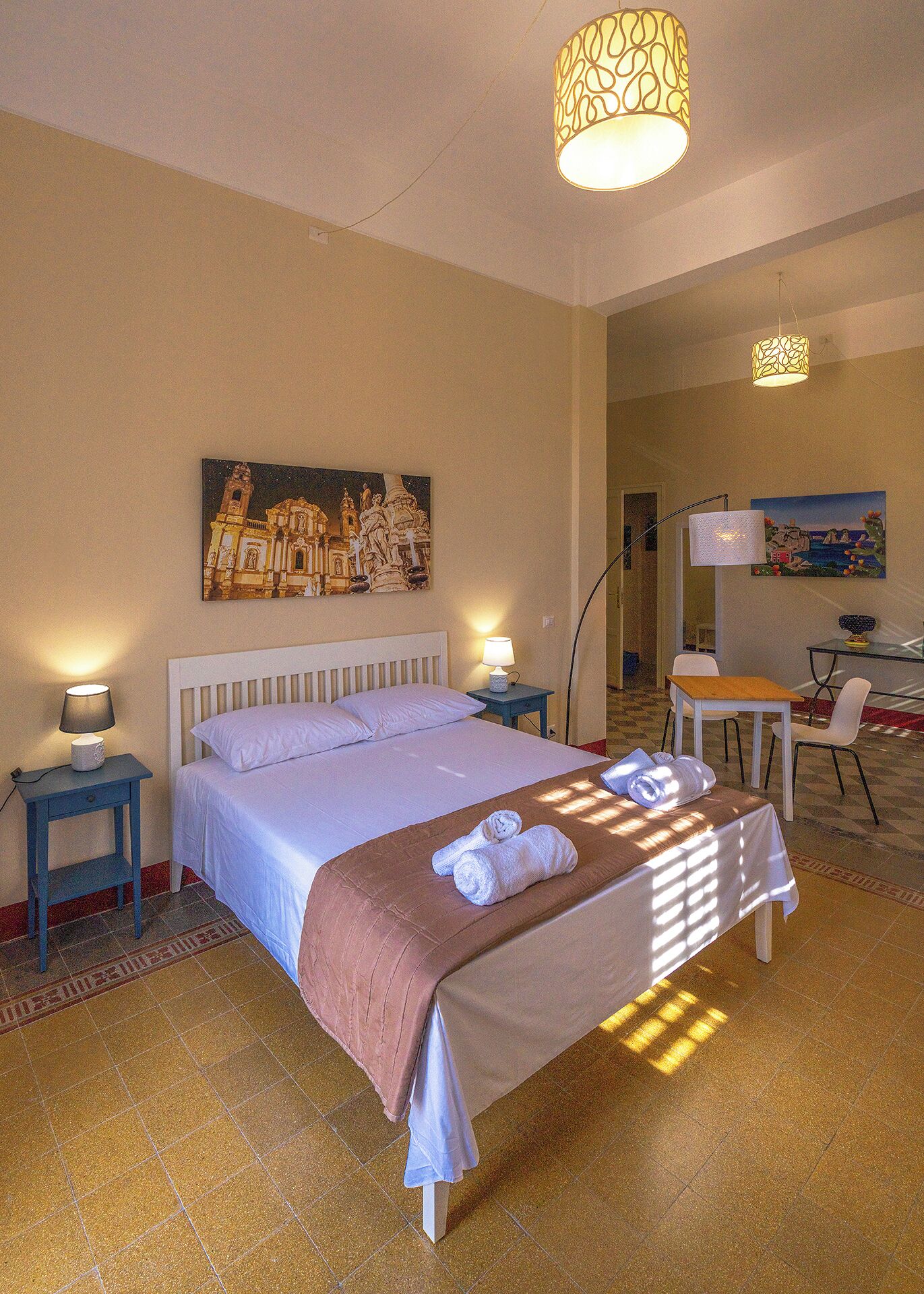 Ein Hotelzimmer mit einem Bett, zwei Nachttischlampen, einem Gemälde an der Wand, einem Schreibtisch mit Stuhl und einem Tisch.