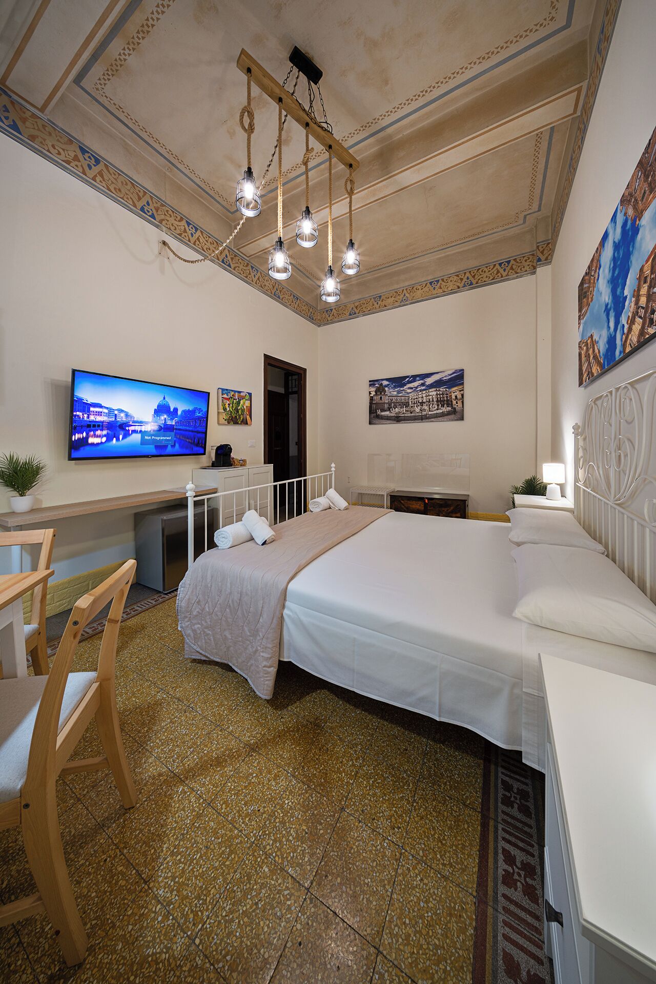 A hotel room with a large bed, a desk with a TV, a fireplace, and a ceiling with a decorative design.