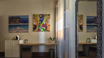 A hotel bathroom with a large mirror, a sink, a cabinet, a potted plant, and artwork on the walls.