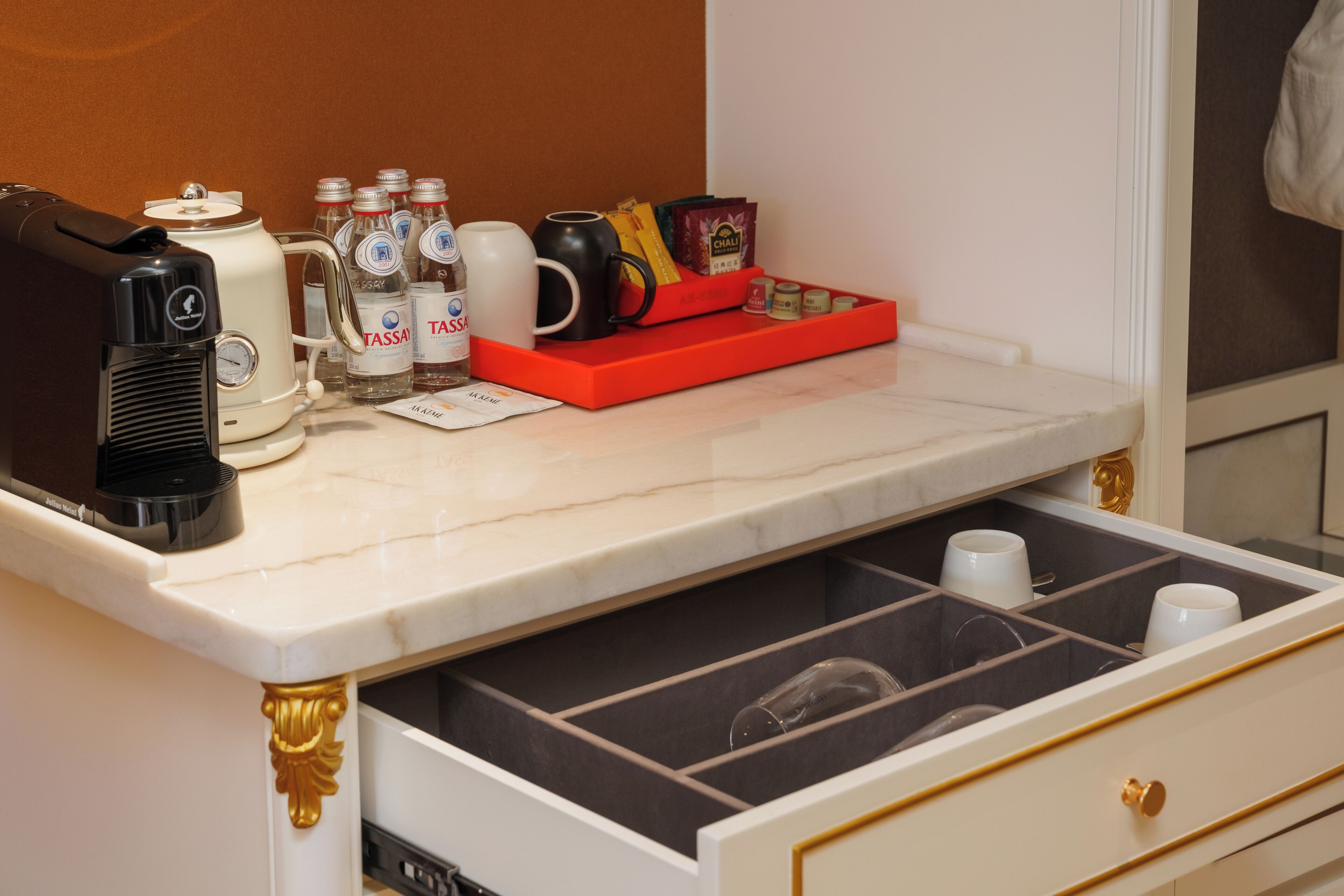 Un comptoir de cuisine avec une machine à café, des bouteilles d’eau, un service à thé et un plateau rouge contenant des en-cas.