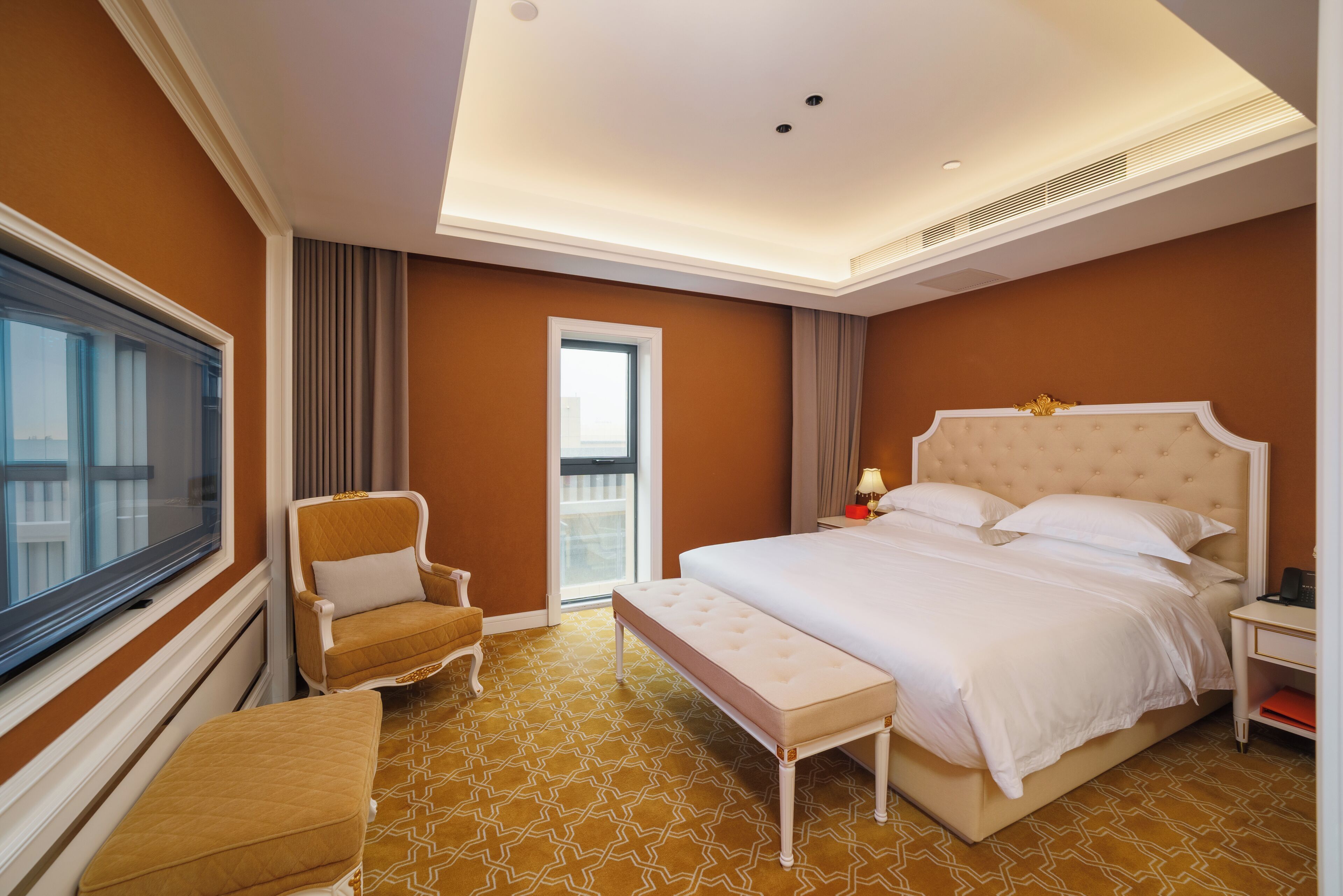 A hotel room with a large bed, a chair, a bench, a nightstand, and a window.