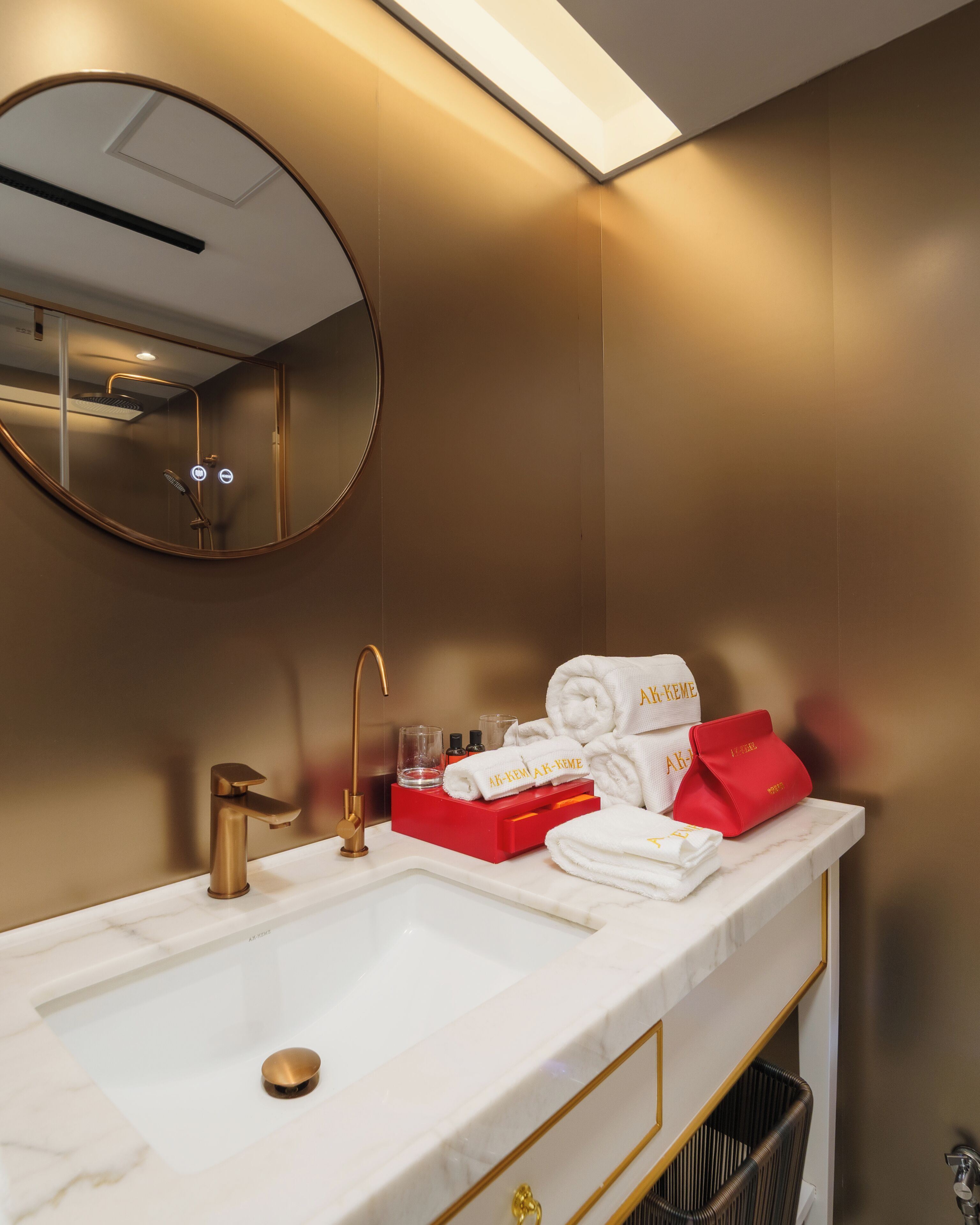 Un baño de hotel con un lavamanos blanco, detalles dorados, un espejo redondo y toallas y artículos de aseo personales ordenados.