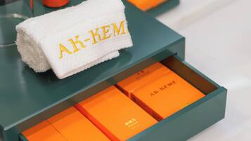 Una caja color aguamarina con una toalla blanca etiquetada 'AK-KEM' y tres cajas naranjas en su interior.