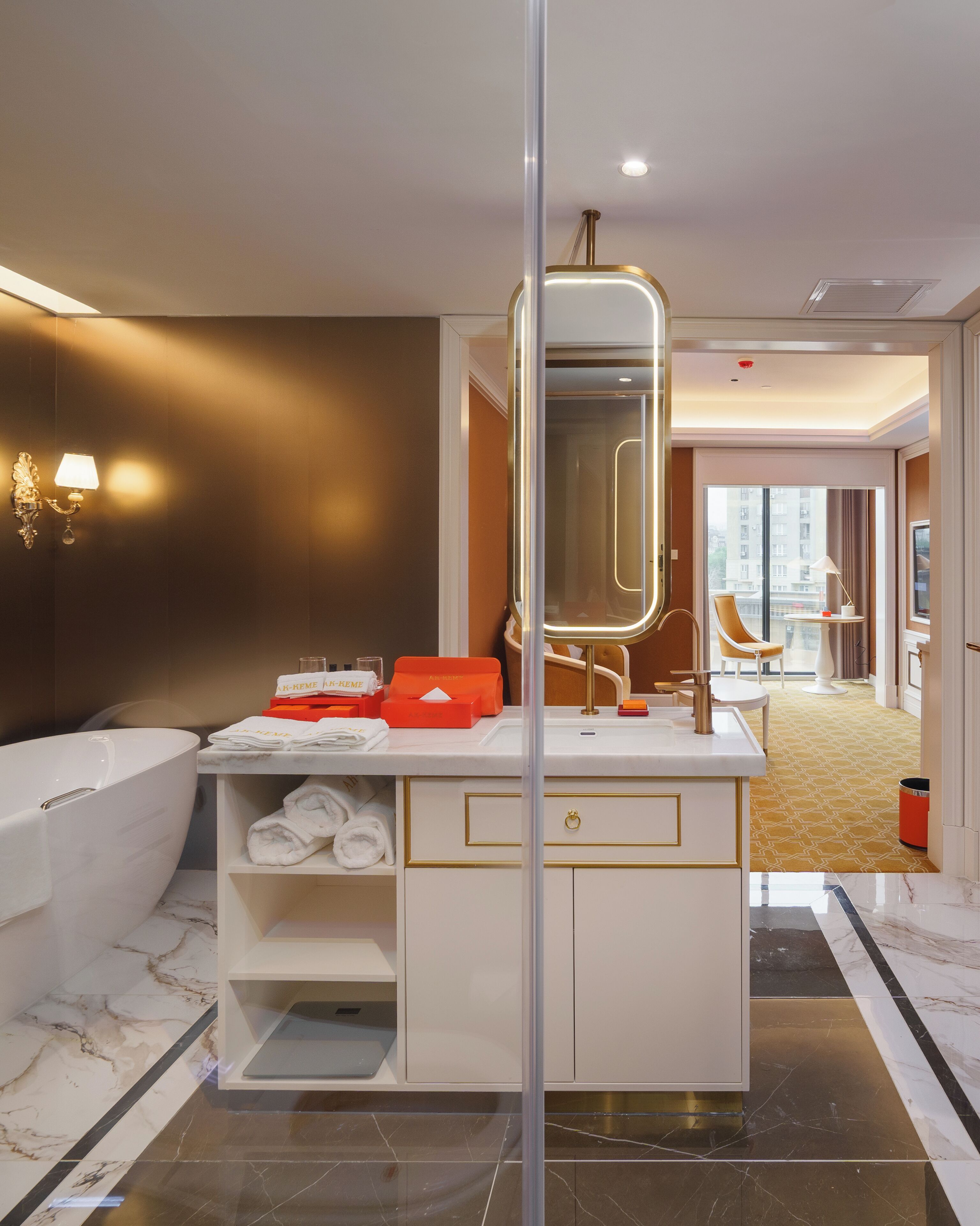 Ein modernes Badezimmer mit freistehender Badewanne, einem Waschtisch mit Spiegel und Blick ins Hotelzimmer.
