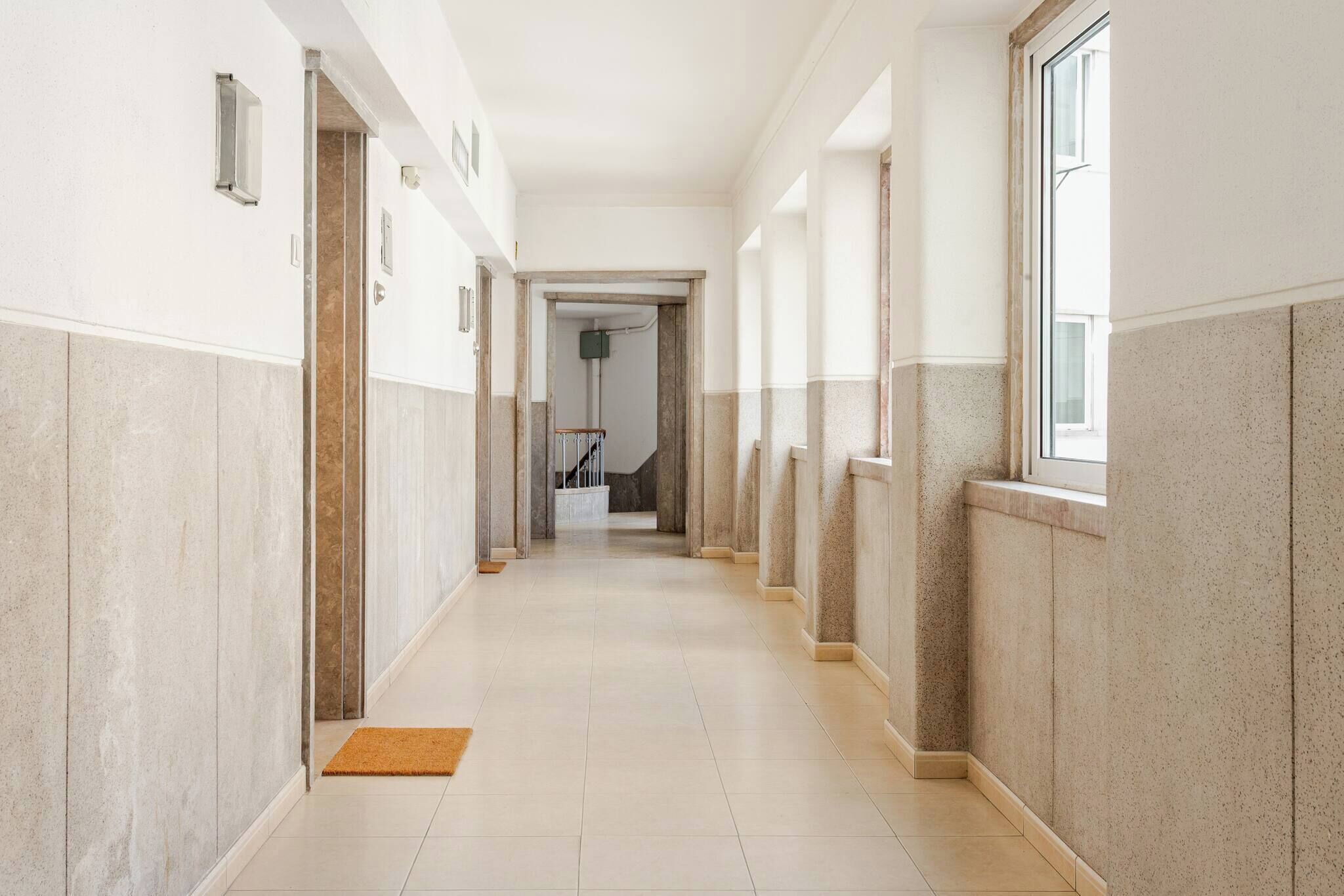 Ein langer, schmaler Korridor mit Fliesenboden und -wänden, der zu einer Treppe führt.