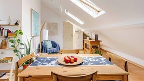 A cozy dining area with a wooden table, a plate of apples, and a blue patterned tablecloth. There are potted plants, a bookshelf, and a painting on the wall. - Trendy Loft Heart Of The City! (Lisboa)