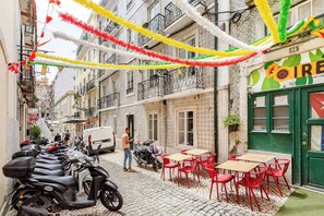 A narrow street with cobblestone pavement, parked scooters, and a café with red chairs and tables. - Trendy Loft Heart Of The City! (Lisboa)