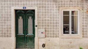 A building facade with a double green door, a window with a grid pattern, and a tiled wall with a repeating geometric design. - Trendy Loft Heart Of The City! (Lisboa)