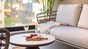 En balkon med et rundt bord, en fletsofa og udsigt over byen.