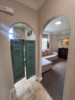 A hallway with two green doors, a sofa, and a lamp in a room with a tiled floor and a fireplace. - Cozy Studio Flat in South Croydon - Ideal for Short or Long Stays (Croydon)