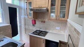 A compact kitchen with wooden cabinets, a gas stove, and a dishwasher. - Cozy Studio Flat in South Croydon - Ideal for Short or Long Stays (Croydon)