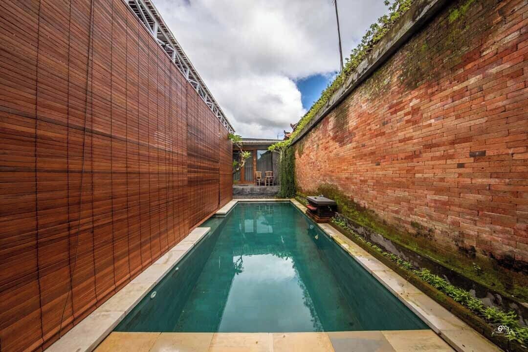 A narrow swimming pool with a wooden wall on one side and a brick wall on the other, with a clear sky above.