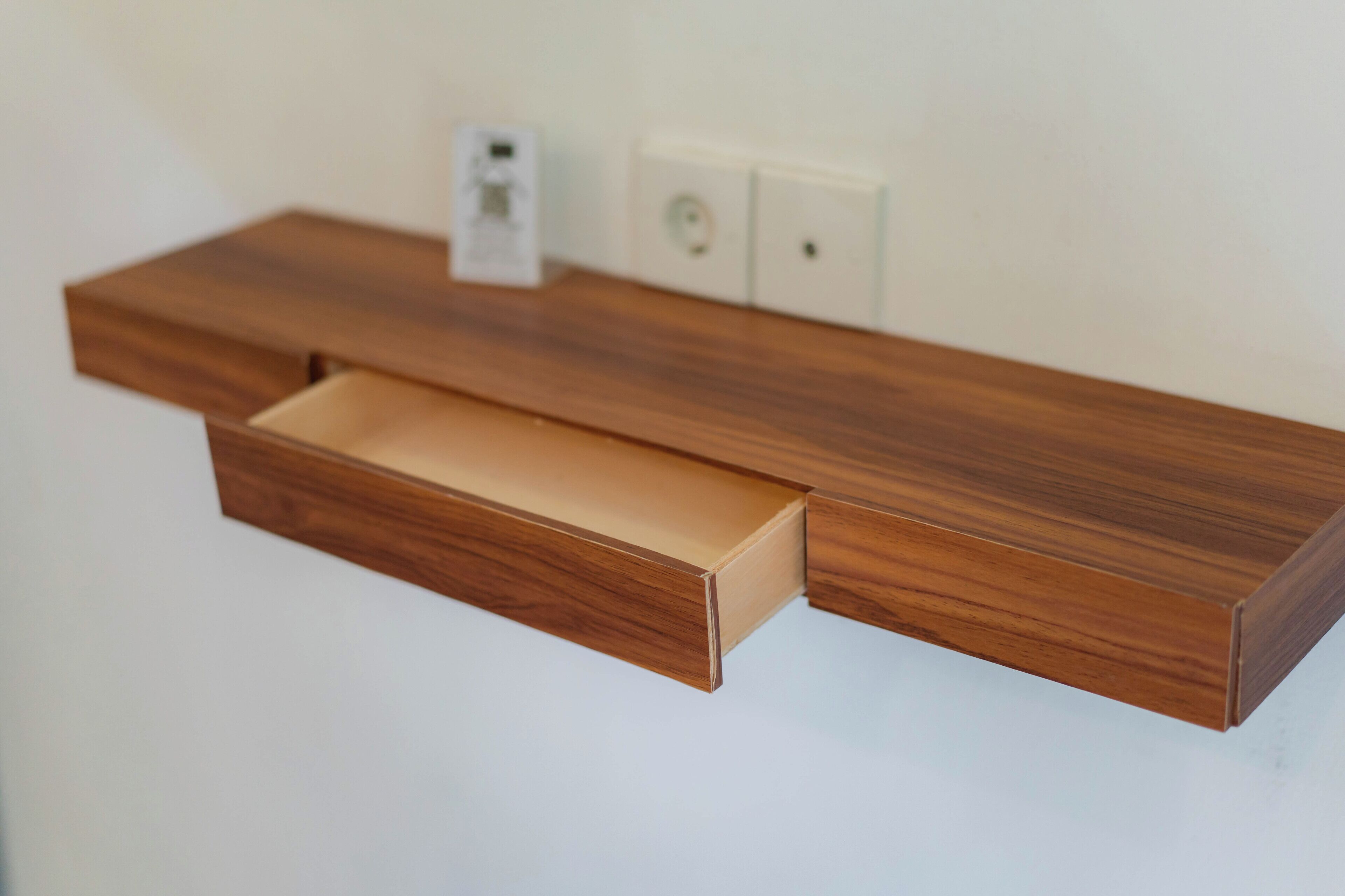 A wooden shelf with a drawer, a power outlet, and a light switch on the wall.