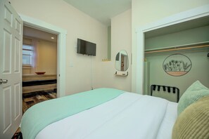 A bedroom with a bed, a television mounted on the wall, a mirror, and a closet with a circular mirror and a decorative plate.
