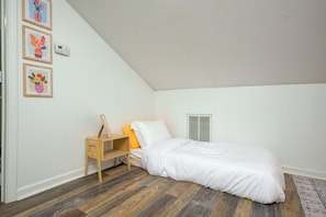 A bedroom with a sloped ceiling, a bed with white bedding, a bedside table with a picture frame, and a wall-mounted heater. - HotTub~FirePit~Games~YogaNook~5 Mins to Downtown (Indianapolis)