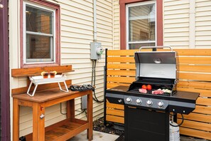 An outdoor barbecue setup with a grill, a wooden table with drinks, and a bench. - HotTub~FirePit~Games~YogaNook~5 Mins to Downtown (Indianapolis)