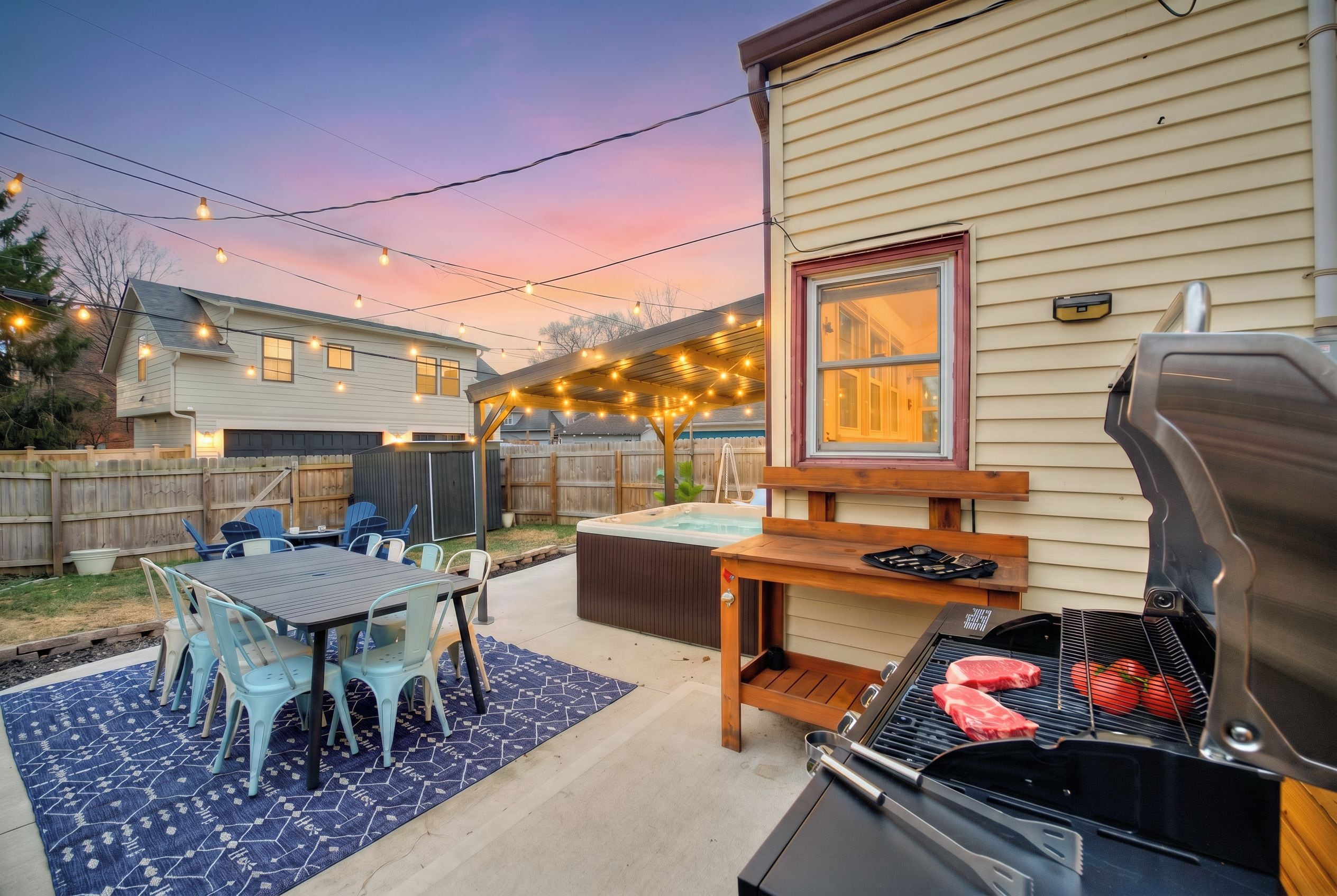 Un jardin avec un barbecue, des meubles pour s’asseoir à l’extérieur et des guirlandes lumineuses.