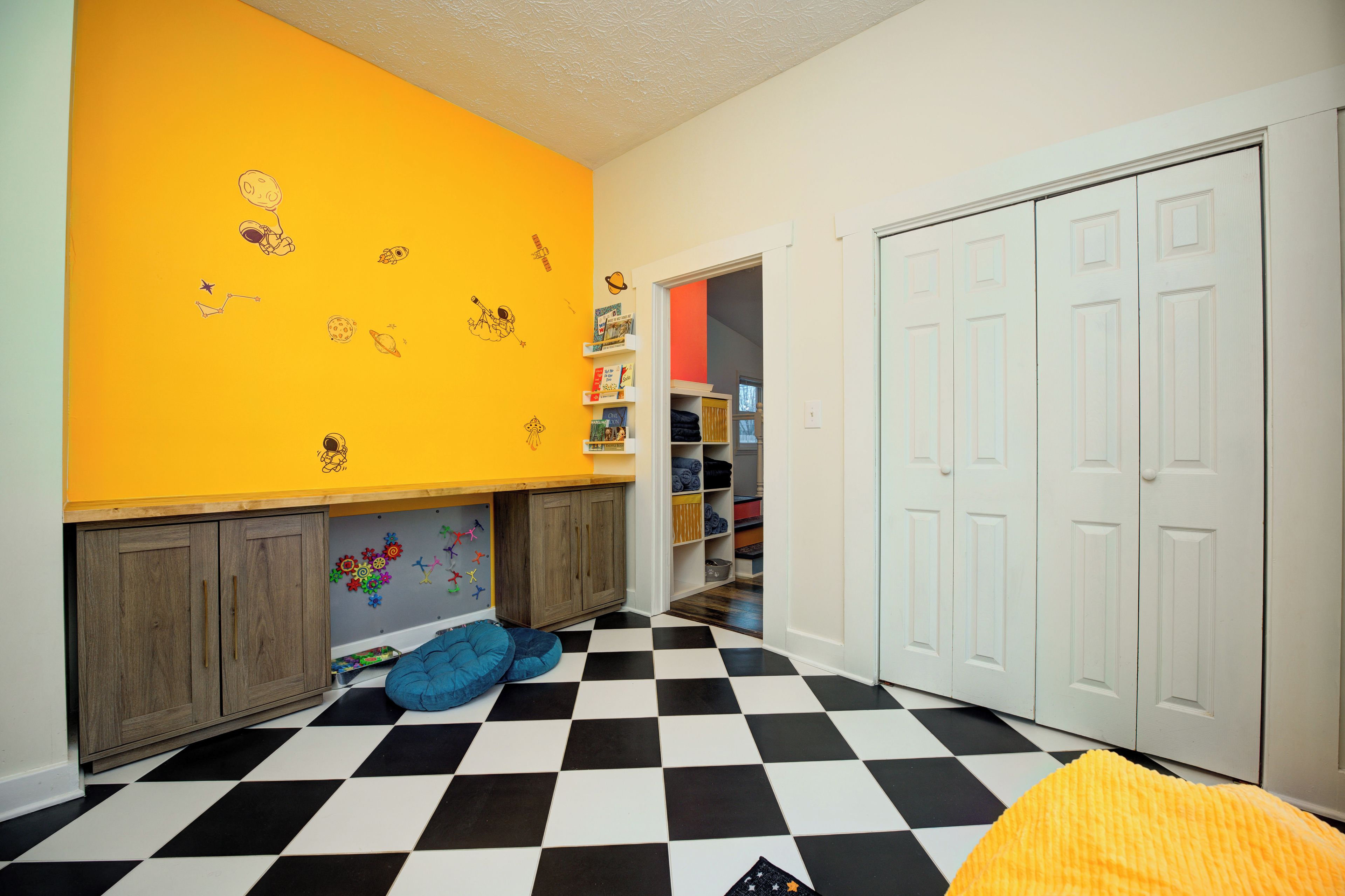 Une chambre d’enfant avec un sol à carreaux, une armoire et une bibliothèque remplie de livres.