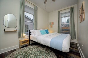 A bedroom with a bed, a bedside table, a lamp, a mirror, and a window with curtains.