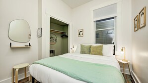 Una camera da letto ordinata con un letto, un comodino, una lampada e un armadio pieno di vestiti.