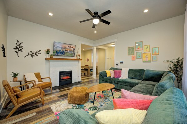 A living room with a fireplace, a ceiling fan, and a sofa with colorful cushions.