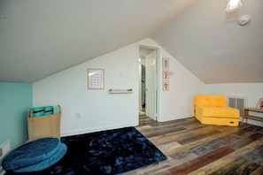 A room with a sloped ceiling, a wooden floor, a blue rug, a yellow sofa, and a basket with items.