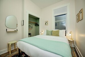 Ein Schlafzimmer mit Bett, Nachttischen, einem Spiegel, einem Kleiderschrank und einem Fenster.