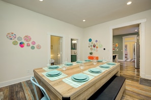 A dining area with a long table set for six, surrounded by chairs, with a kitchen in the background. - HotTub~FirePit~Games~YogaNook~5 Mins to Downtown (Indianapolis)