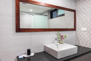 Un baño con un espejo grande, un lavamanos blanco y una encimera negra.