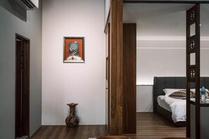 Habitación de hotel moderna con piso de madera, cama con ropa blanca, un pequeño florero y un cuadro en la pared.