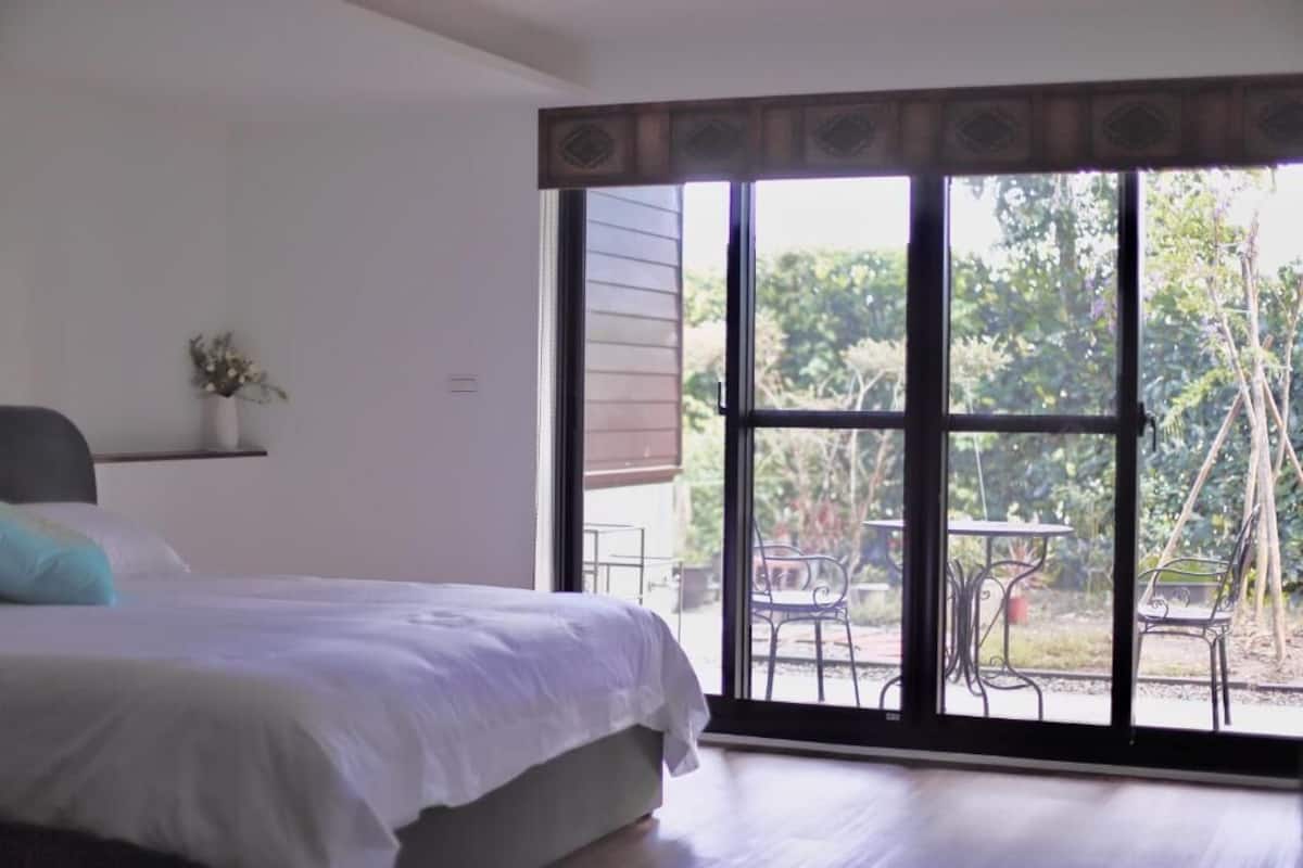A bedroom with a bed, a small table with chairs, and a window with a view of the outdoors.