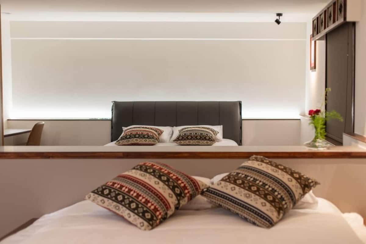 A modern hotel room with a large bed, a dark headboard, and decorative pillows.