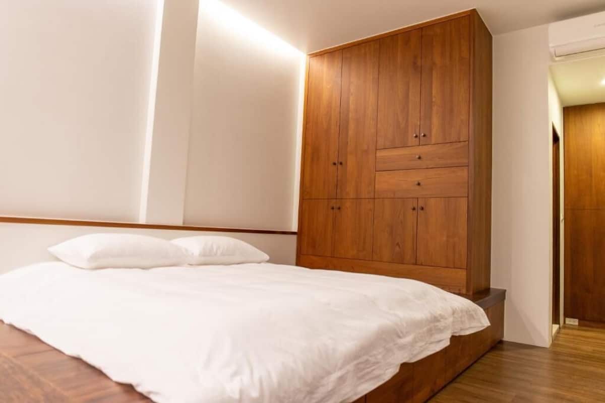 A bedroom with a wooden wardrobe, a bed with white bedding, and a wooden floor.