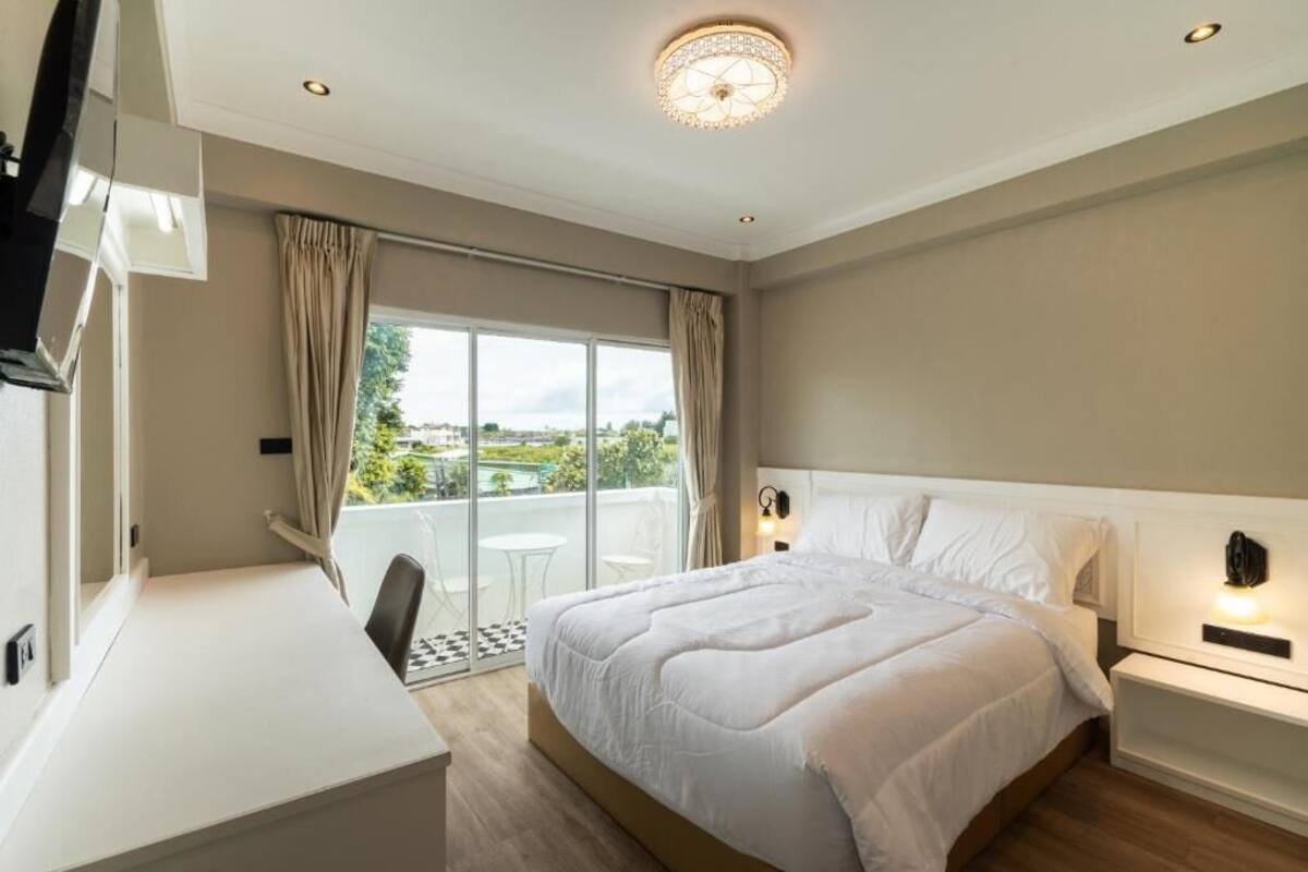 A hotel room with a large bed, a desk, and a balcony with a view.