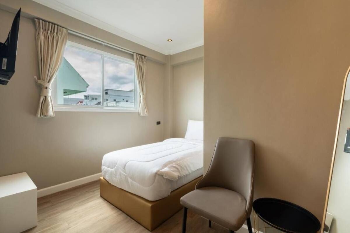 A modern hotel room with a bed, a chair, a small table, and a window with curtains.