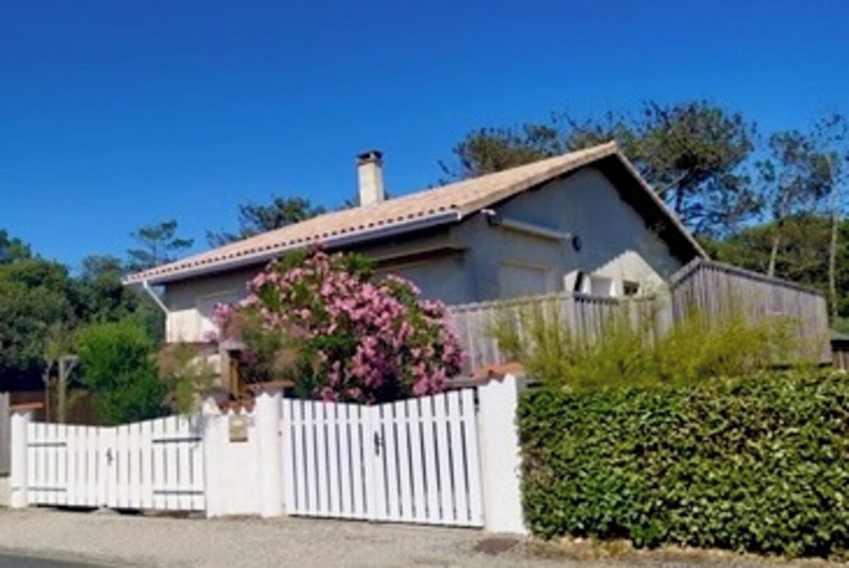 Ein Haus mit weißem Zaun, einem Garten voller rosa Blumen und einem strahlend blauen Himmel.